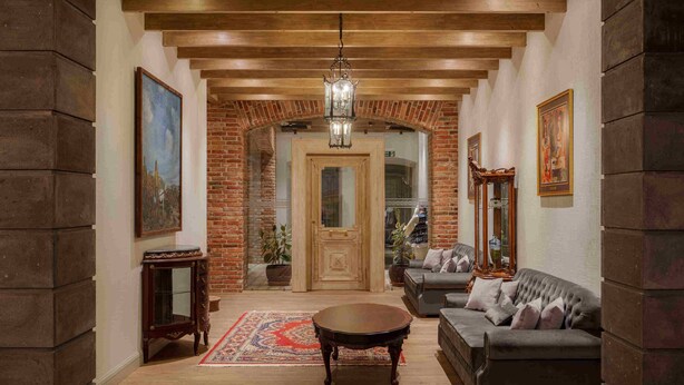 A spacious living room with a wooden ceiling, a large sofa, a coffee table, and a chandelier. - Grand Hotel Gyumri  (Gyumri)