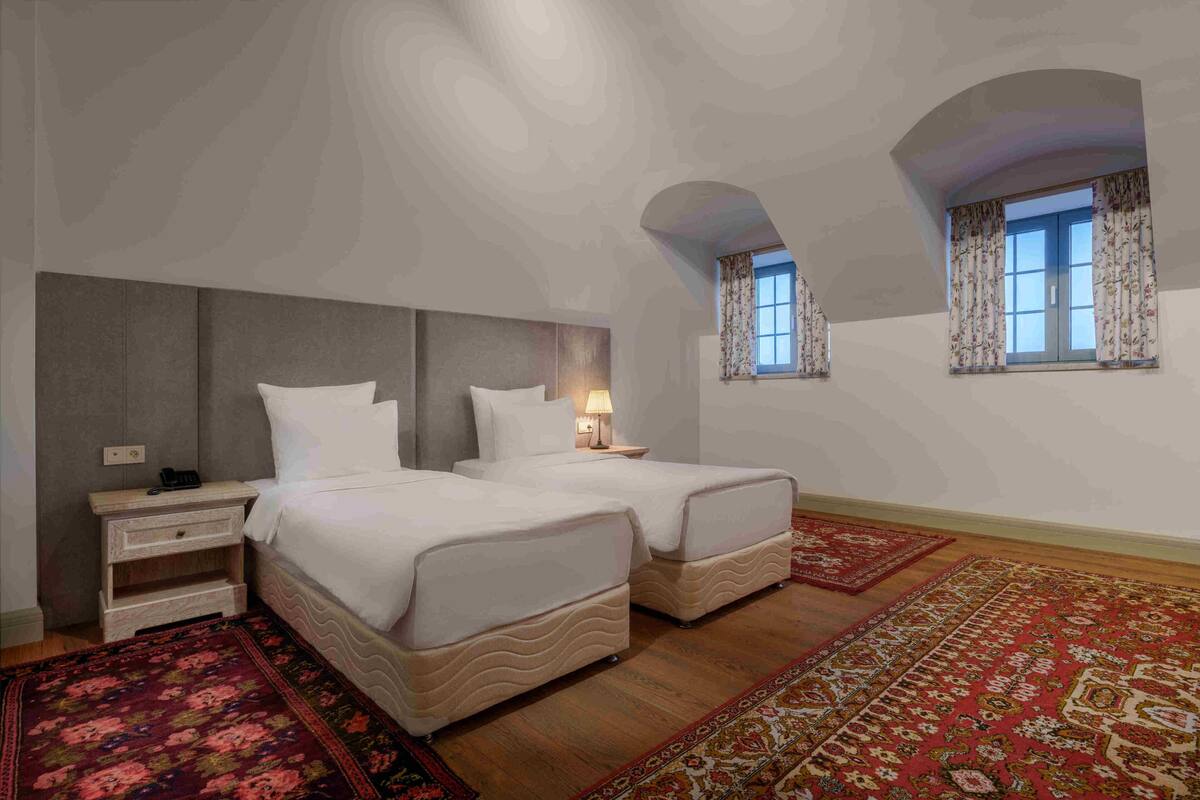Une chambre avec deux lits, une table de chevet, une lampe et une fenêtre avec des rideaux.