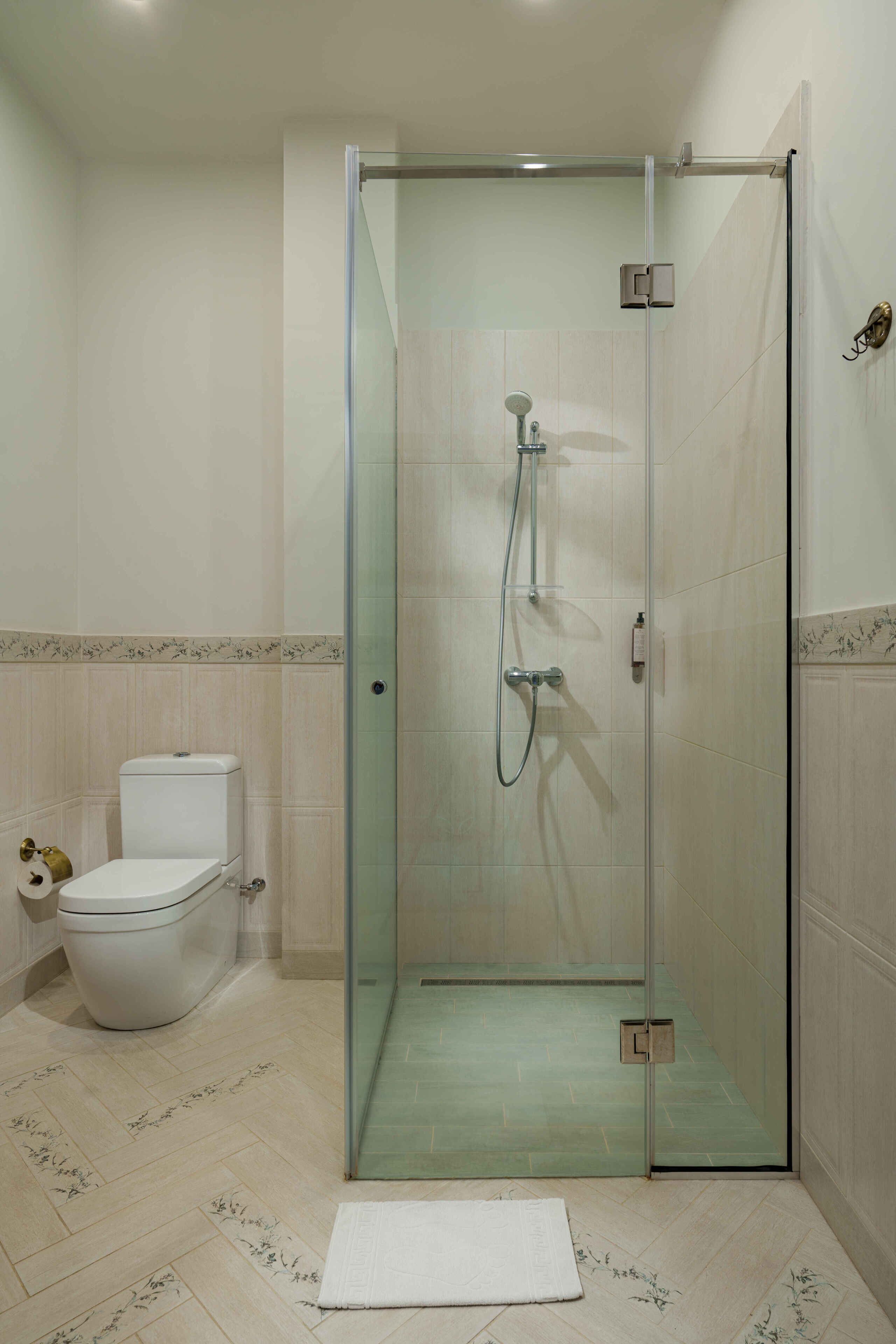 A modern bathroom with a glass-enclosed shower, a toilet, and a white rug on the floor.