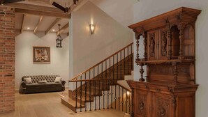 A wooden staircase with a wrought iron railing, a dark brown sofa, and a wooden cabinet with intricate carvings. - Grand Hotel Gyumri  (Gyumri)