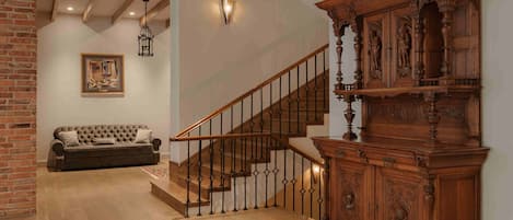 Una escalera de madera con barandilla de hierro forjado, un sofá marrón oscuro y un aparador de madera con intrincados grabados.