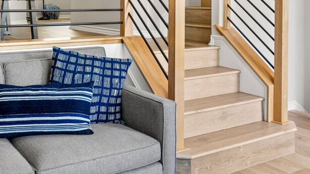 Een moderne woonkamer met een grijze bank, een houten trap en een logo op de muur.