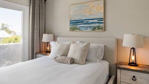 Een hotelkamer met een bed, twee bedlampen, een schilderij van de zee en een raam met gordijnen.