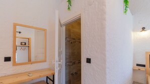 A bathroom with a wooden vanity, a mirror, a shower with a glass door, and a small shelf. - Das Hotel (Çesme)