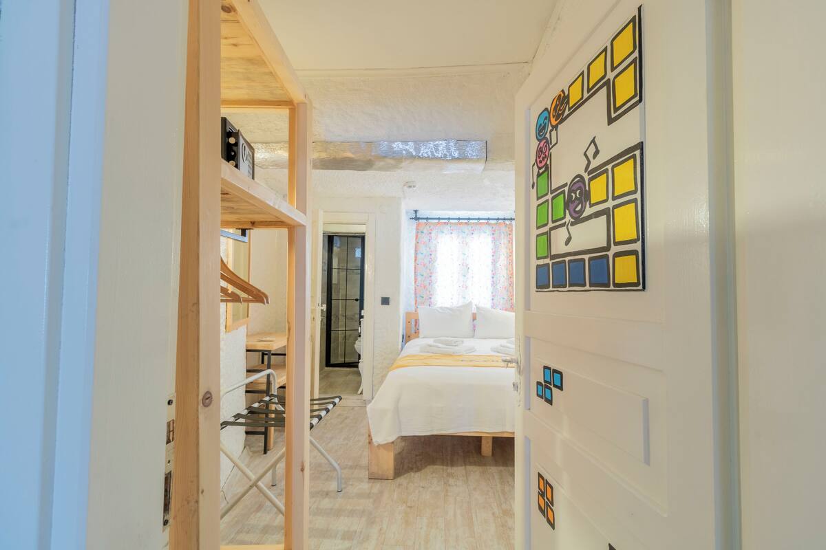 A bedroom with a bed, wooden floor, and a wall with colorful square decorations.