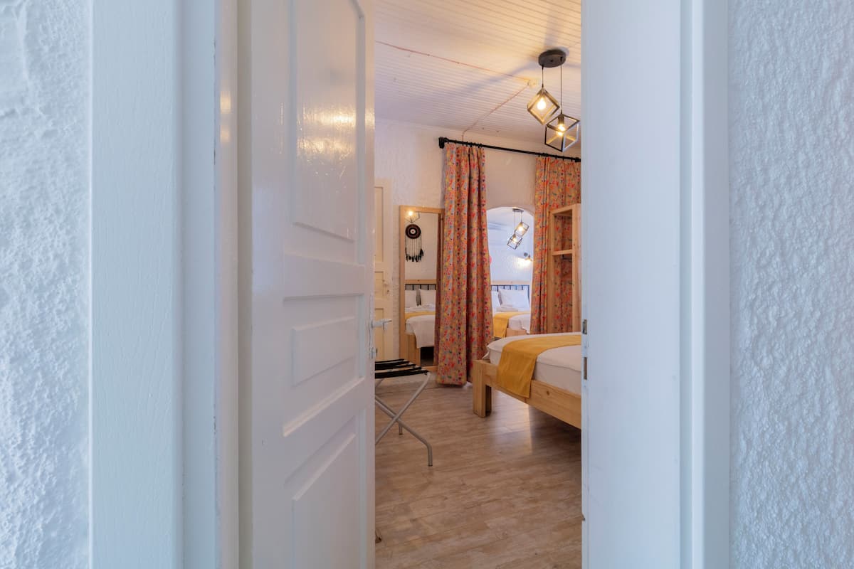 A room with a bed, a desk, and a chair. There is a window with curtains, and a wall-mounted light fixture.