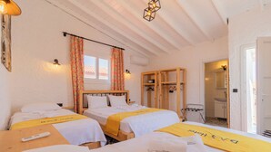A hotel room with two beds, each with a yellow towel and a remote control on the bed. There is a wooden wardrobe and a small table with towels. - Das Hotel (Çesme)