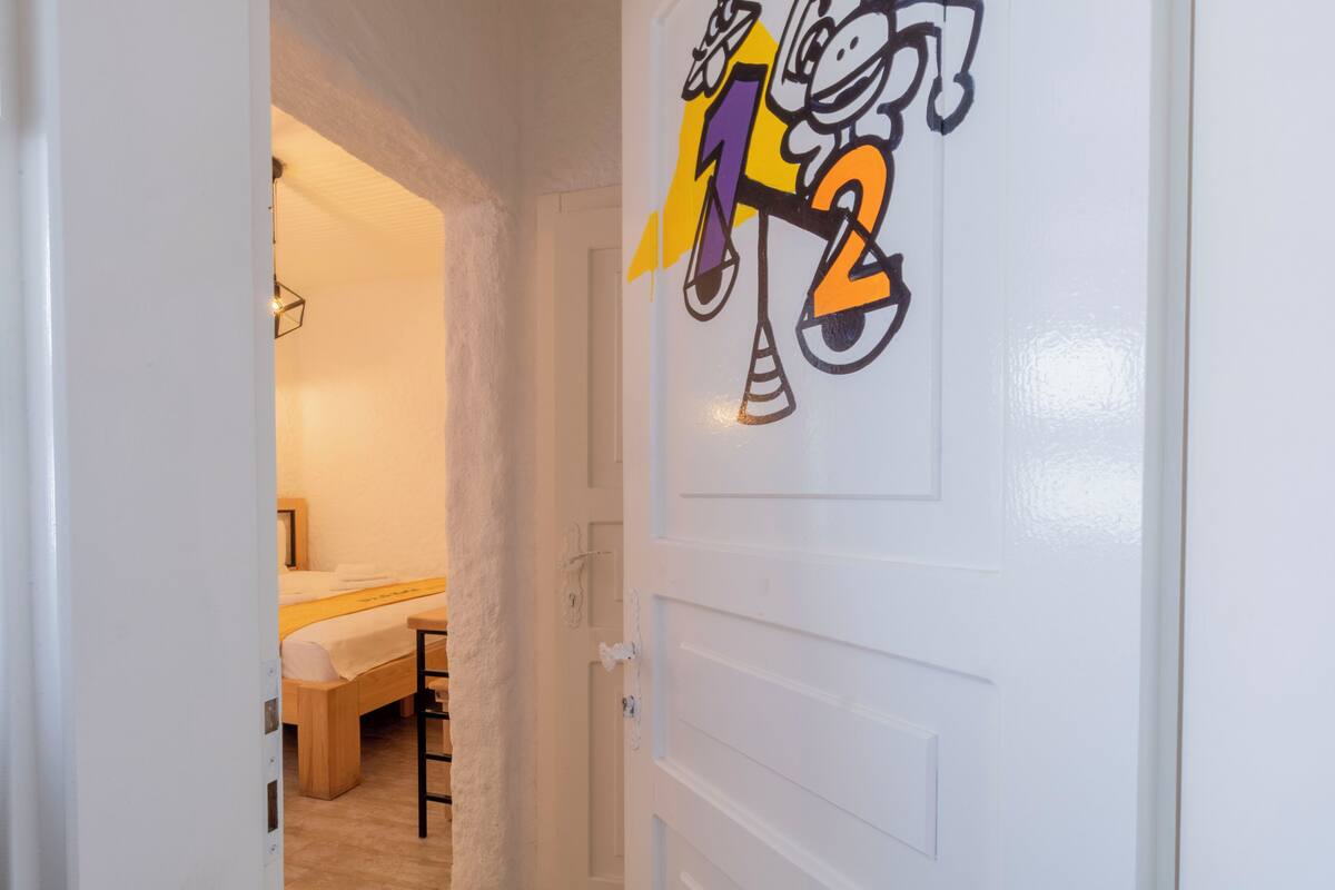 A hotel room with a bed, a bedside table, and a door with a cartoon character design.