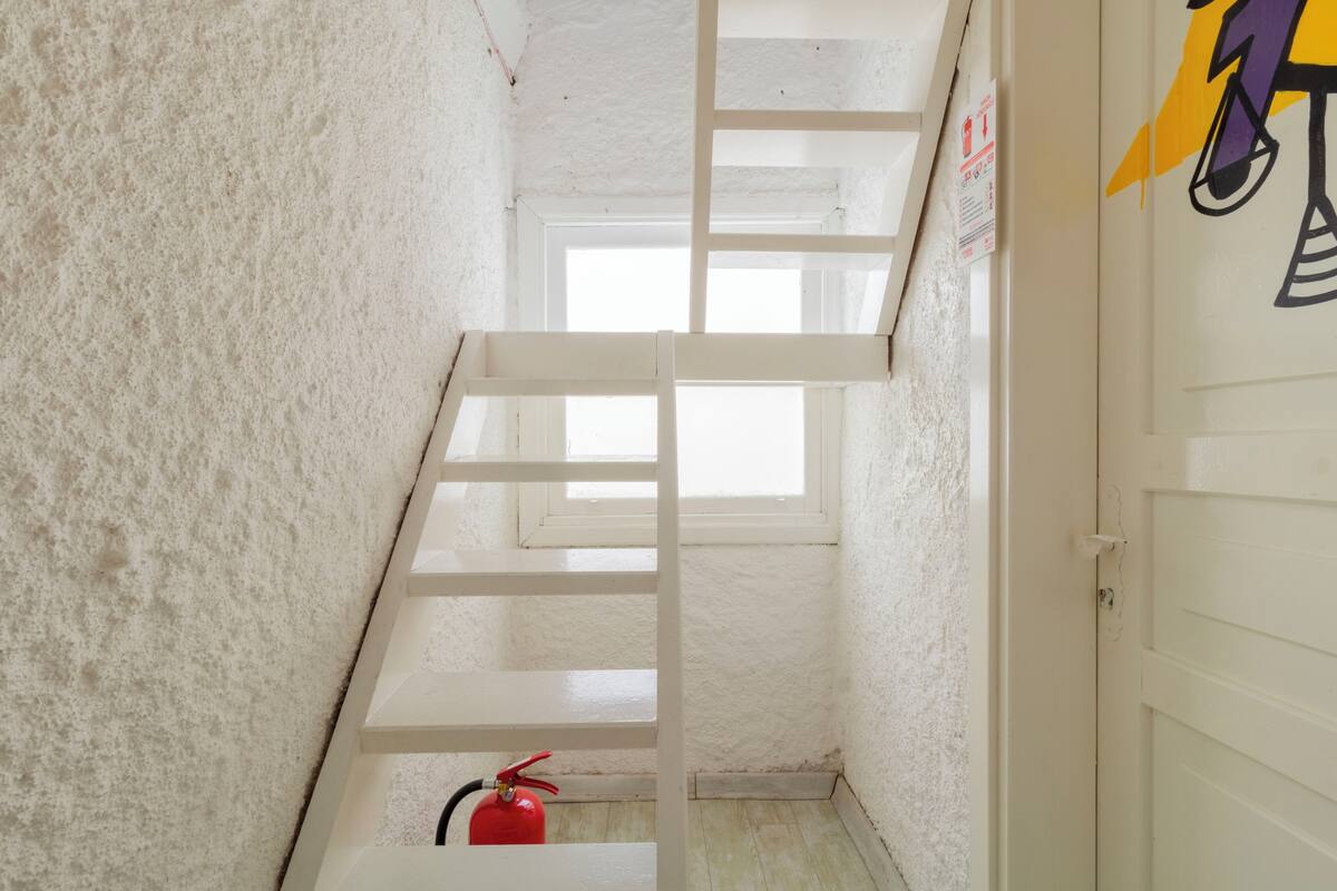 A narrow stairwell with white walls and a fire extinguisher at the bottom.
