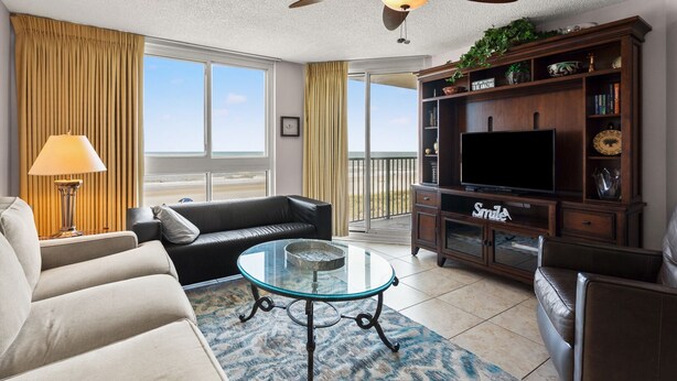 A living room with a sofa, a glass coffee table, a TV, and a bookshelf. - Gorgeous oceanfront vacation rental condo with amazing views and pool (North Myrtle Beach)