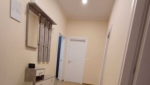Un pasillo con piso de madera, una puerta blanca y un mueble pequeño con espejo y una caja.