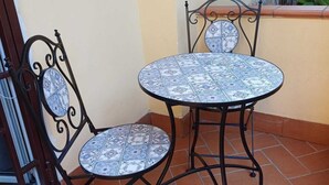 Un pequeño patio al aire libre con una mesa redonda y dos sillas, con piso de baldosas y baranda de metal.