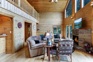 A log cabin interior with a fireplace, a sofa, a chair, and a television. - Scenic Mountain View w/ Hot Tub & Fire Pit (Blue Ridge)