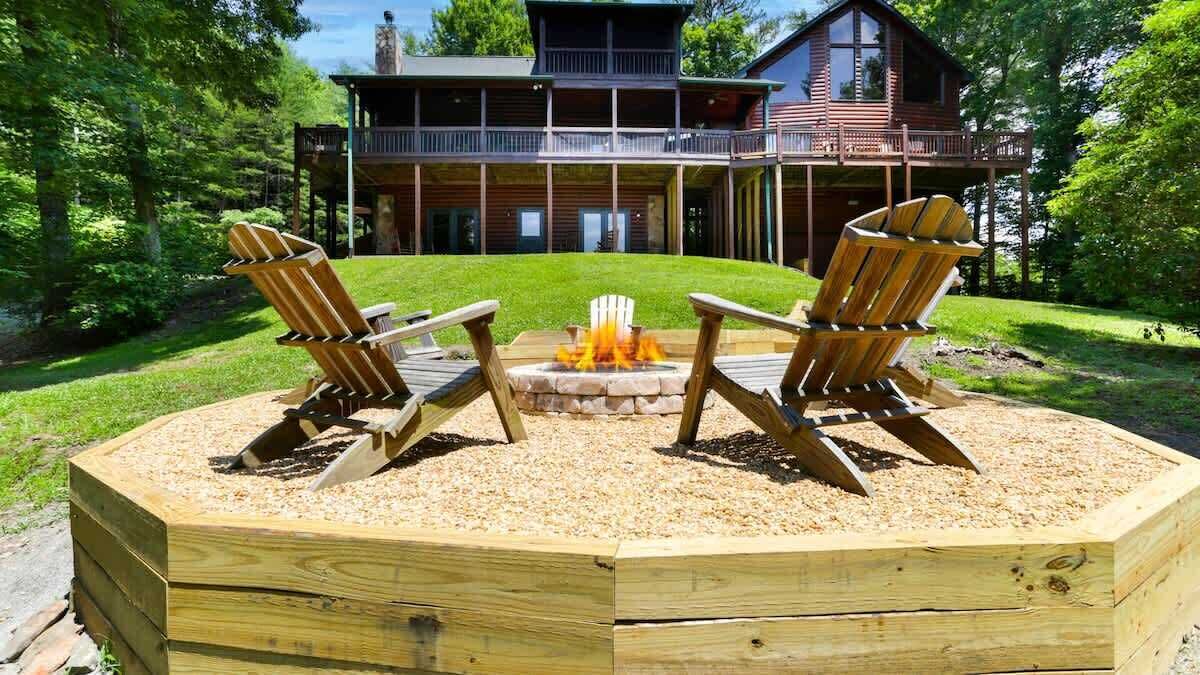 Een houten terras met Adirondack-stoelen en een vuurkuil in het midden, omgeven door een houten terras.