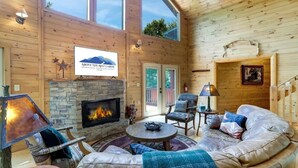 A cozy cabin interior with a stone fireplace, leather sofa, and a sign reading "Above the Rest Cabins." - Scenic Mountain Cabin w/ Hot Tub & Fire Pit (Blue Ridge)