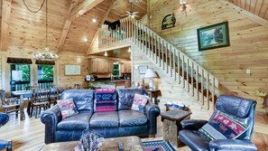 A spacious living room with a leather sofa, a dining area, and a staircase leading to an upper level. - Scenic Mountain View w/ Hot Tub & Fire Pit (Blue Ridge)