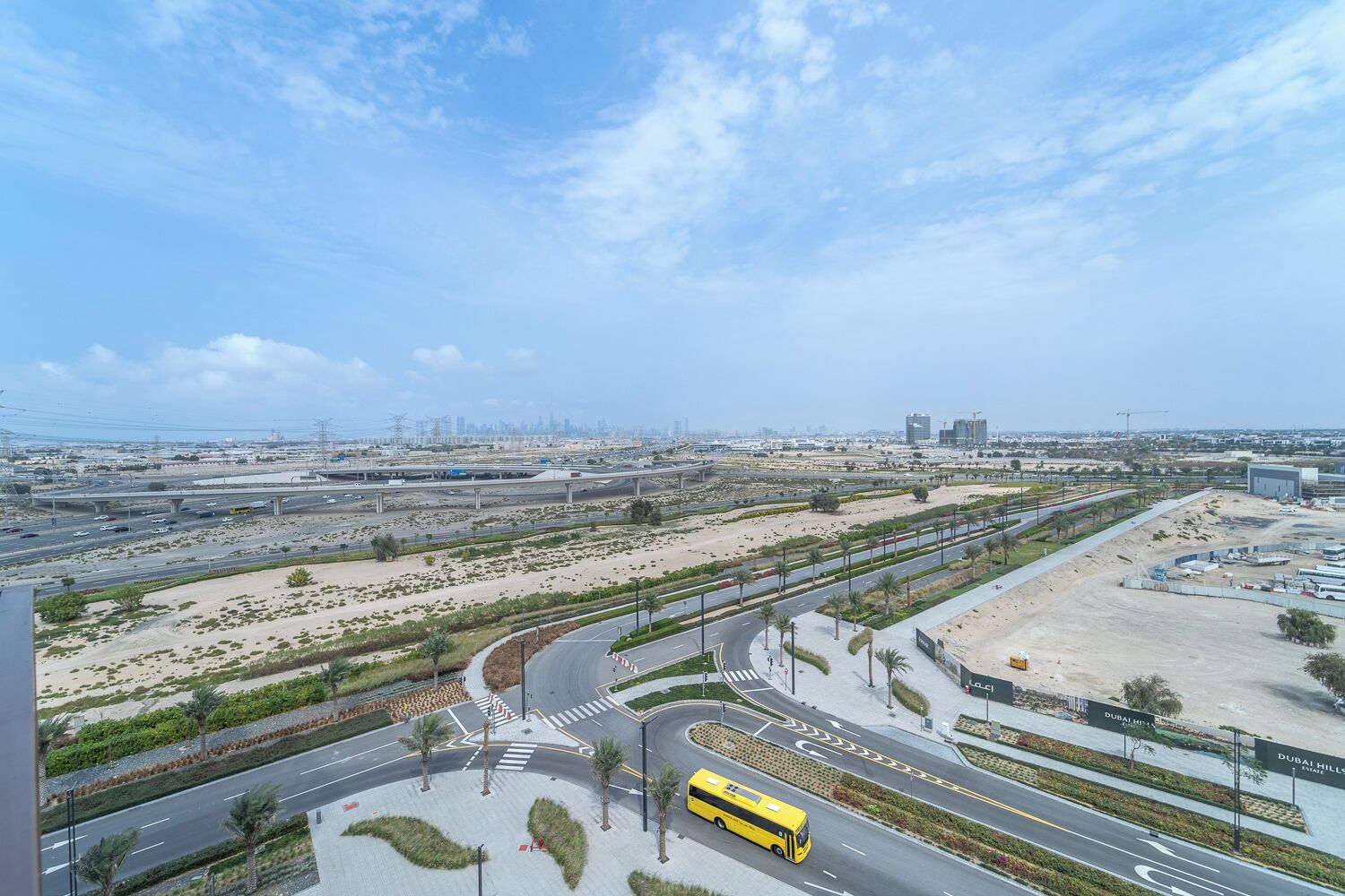 A modern urban landscape with a multi-level highway interchange, a yellow bus, and a large building labeled "Dubai Hills."