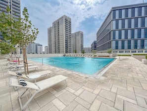 A rooftop pool area with lounge chairs and a swimming pool, surrounded by high-rise buildings. - Cozy 2BD Work in Style Dubai Hills (Dubai)