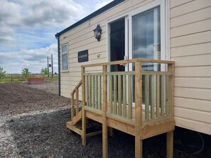 A wooden deck leading to a beige building with a window and a sign reading "The Claremont Suite 67". - 2 Bed Cambridge Lodge (Market Drayton)