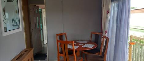 A dining area with a wooden table and chairs, a chandelier, and a view of the outdoors through a window with curtains.