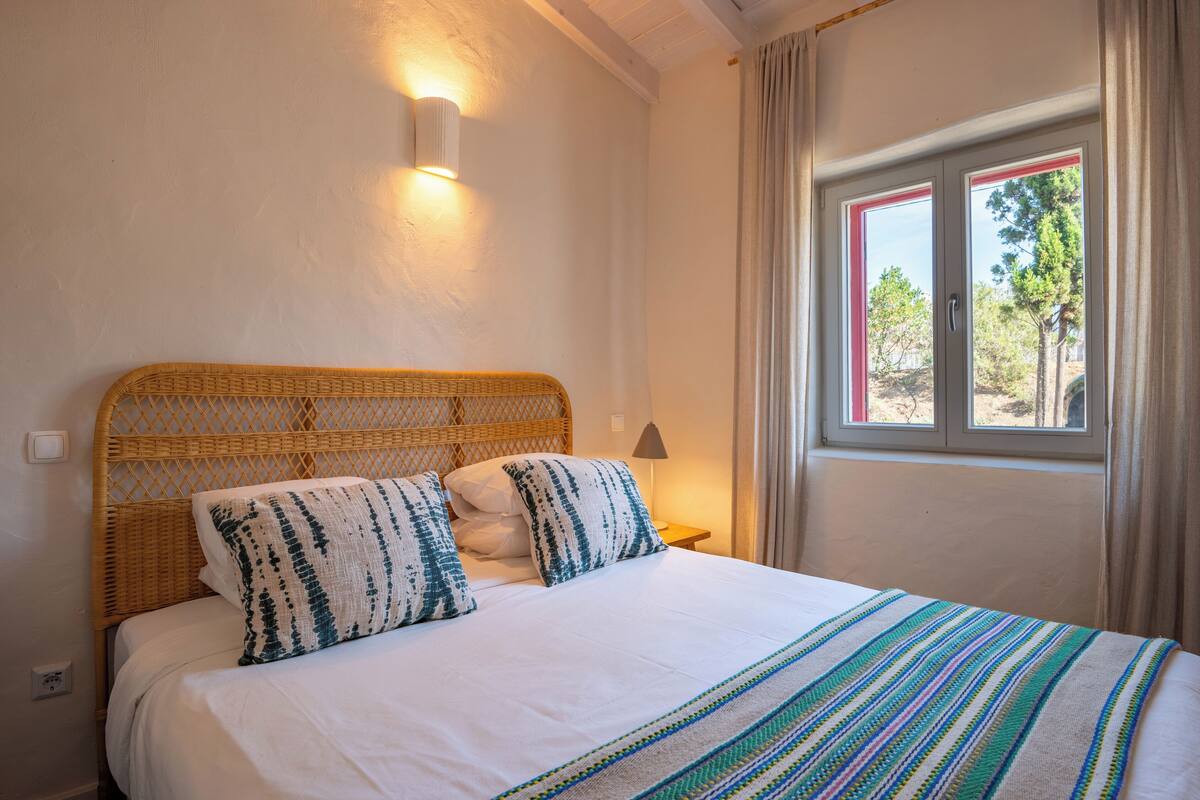 Ein Bett mit einem gewobenen Kopfteil, weißer Bettwäsche und einer gestreiften Decke.