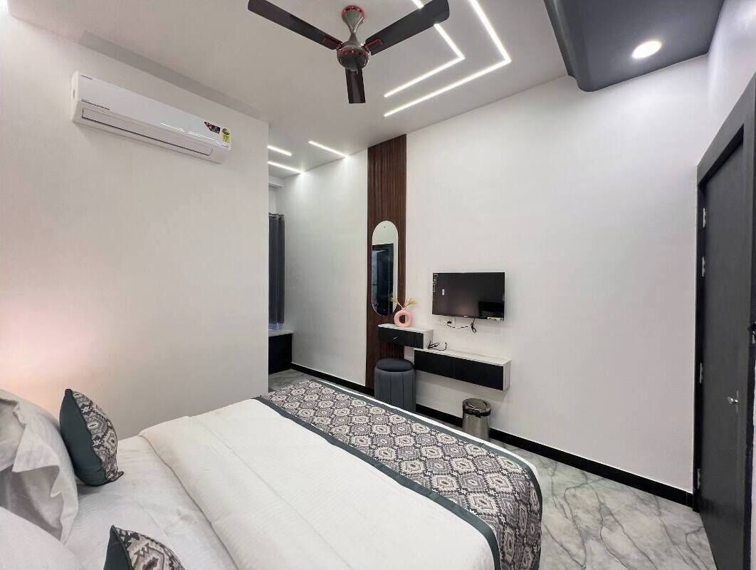 A modern bedroom with a bed, air conditioning unit, ceiling fan, TV, and a mirror.