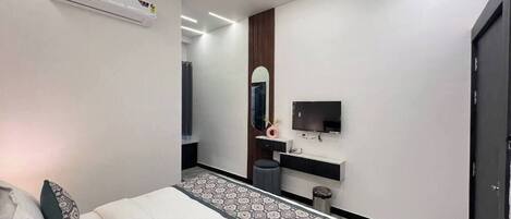 A modern bedroom with a bed, air conditioning unit, ceiling fan, TV, and a mirror.