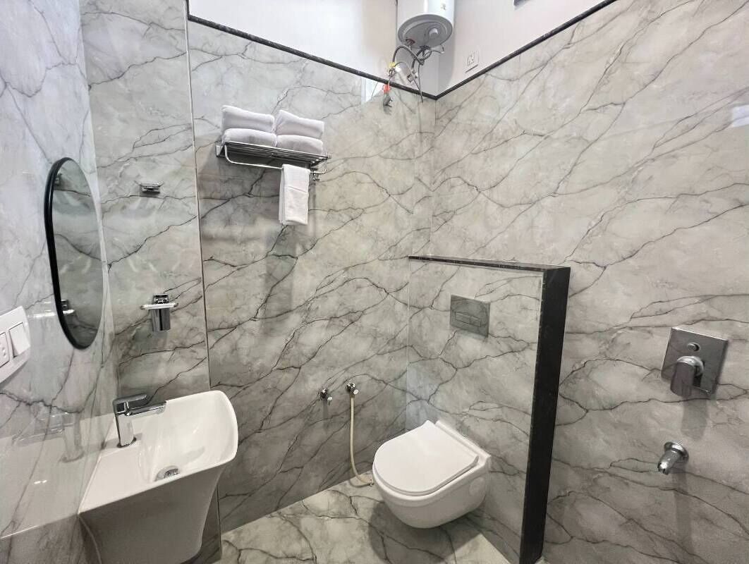 A modern bathroom with a marble wall, a white sink, a toilet, and a shower area.