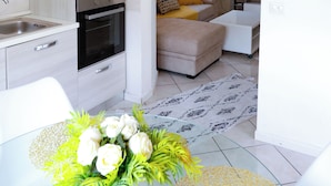 Una cocina moderna con cafetera, horno y lavamanos. Hay un comedor con mesa y sillas, y una sala de estar con sofá y televisor.