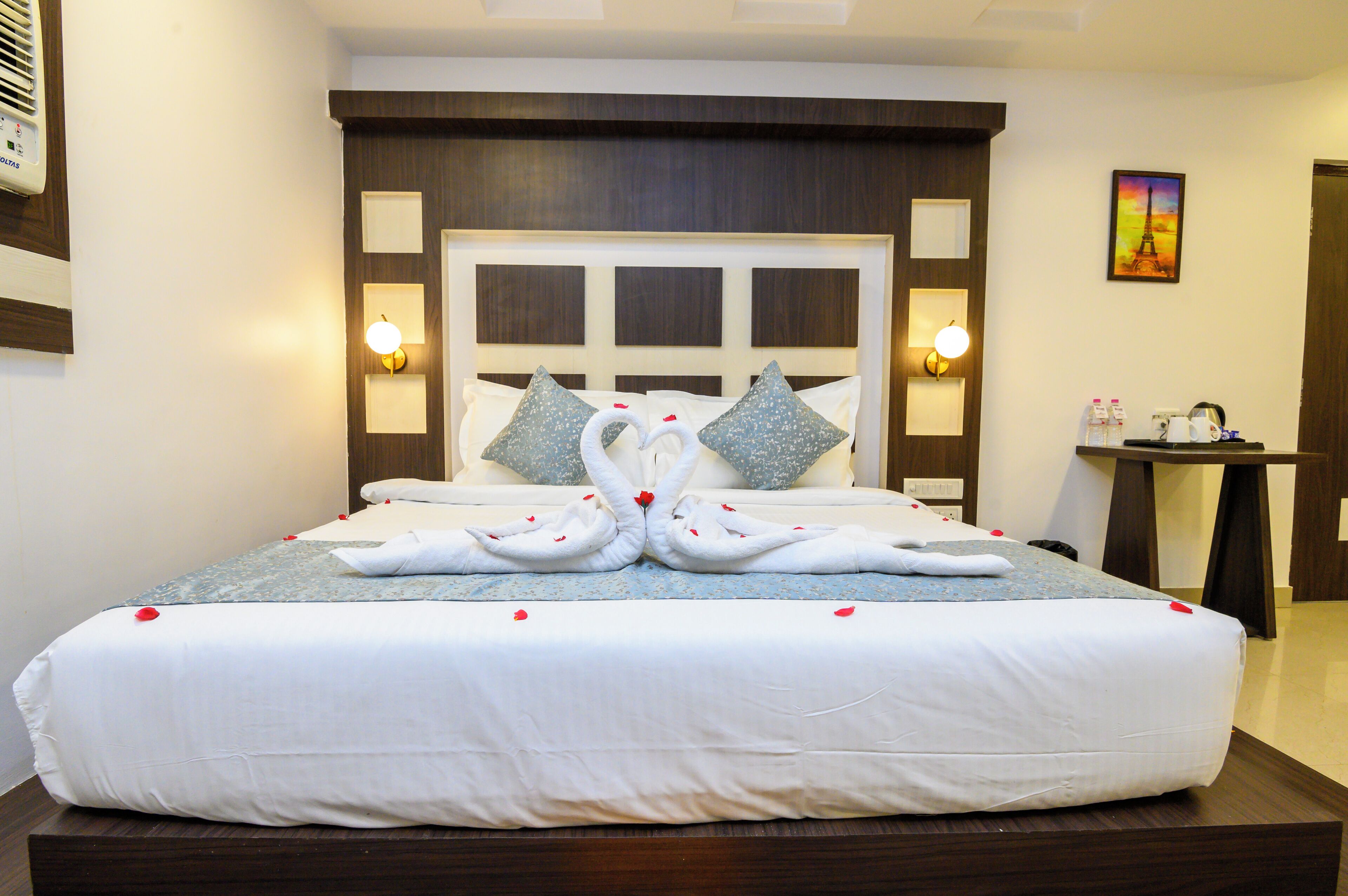 A neatly made bed with a decorative swan design made from towels, a headboard with built-in lighting, and a small table with toiletries.