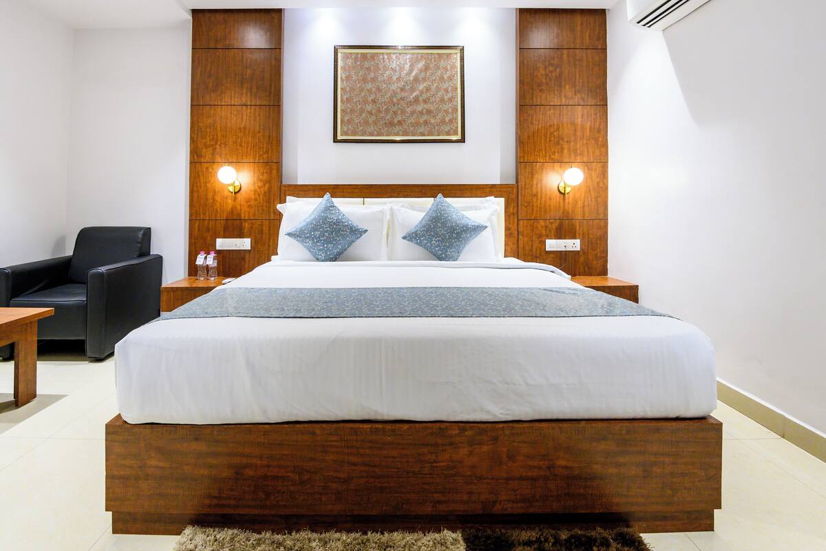 A modern hotel room with a wooden bed frame, two pillows, a bedside table, and a chair.