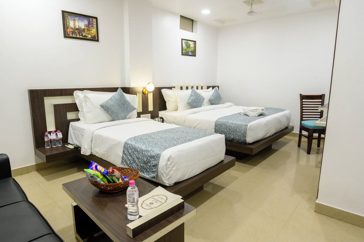 A hotel room with two beds, a desk with a basket of toiletries, and a chair.