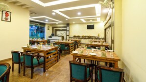 Un restaurante con mesas y sillas de madera, una cocina al fondo, y un techo con iluminación empotrada.