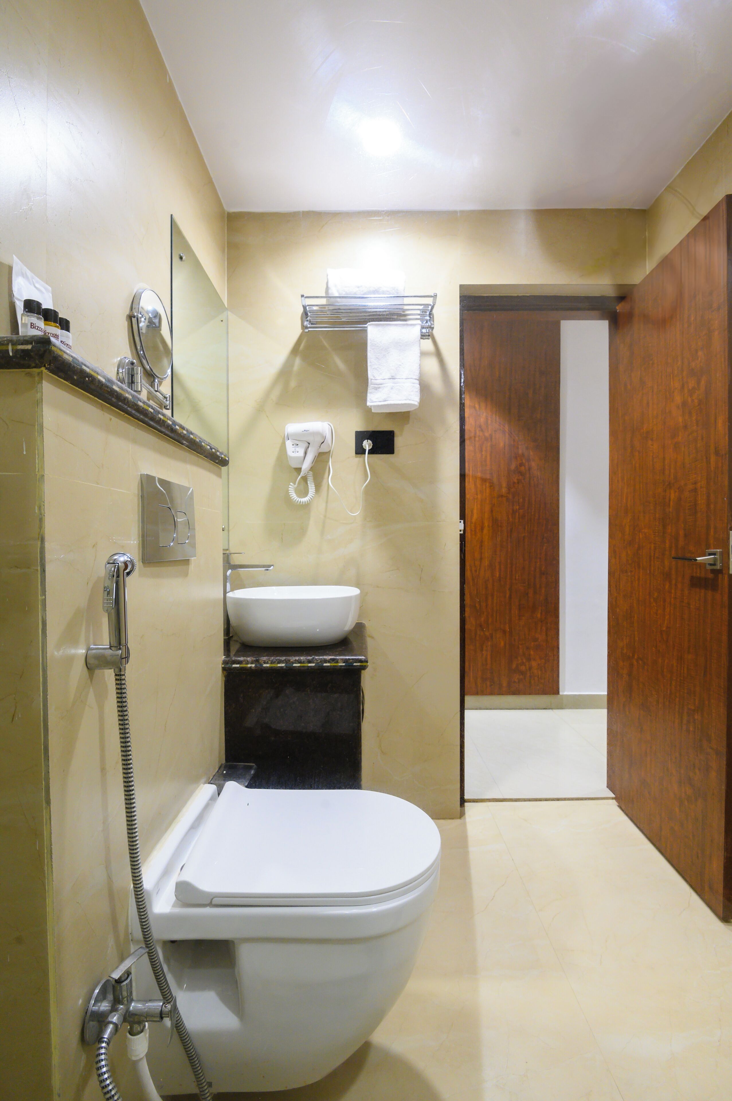 A bathroom with a toilet, sink, and shower. There is a mirror above the sink and a towel rack on the wall.