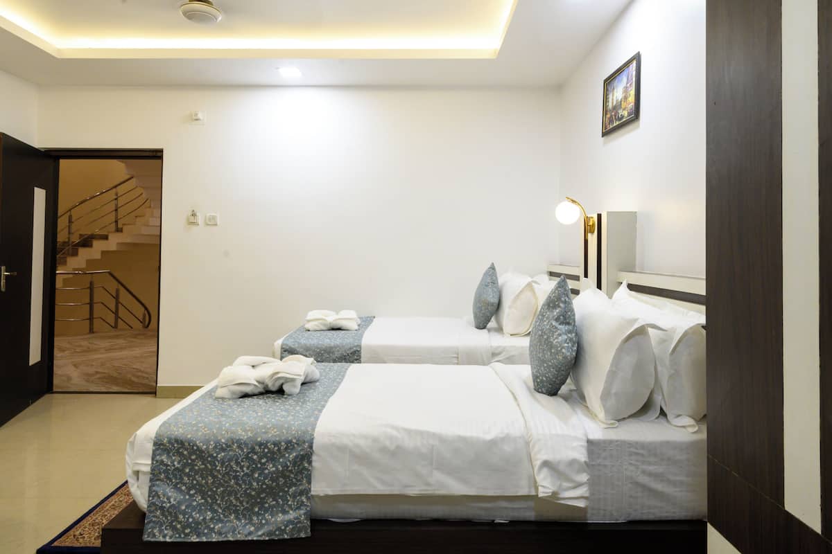 A hotel room with two beds, a staircase, a wall-mounted lamp, and a framed picture.
