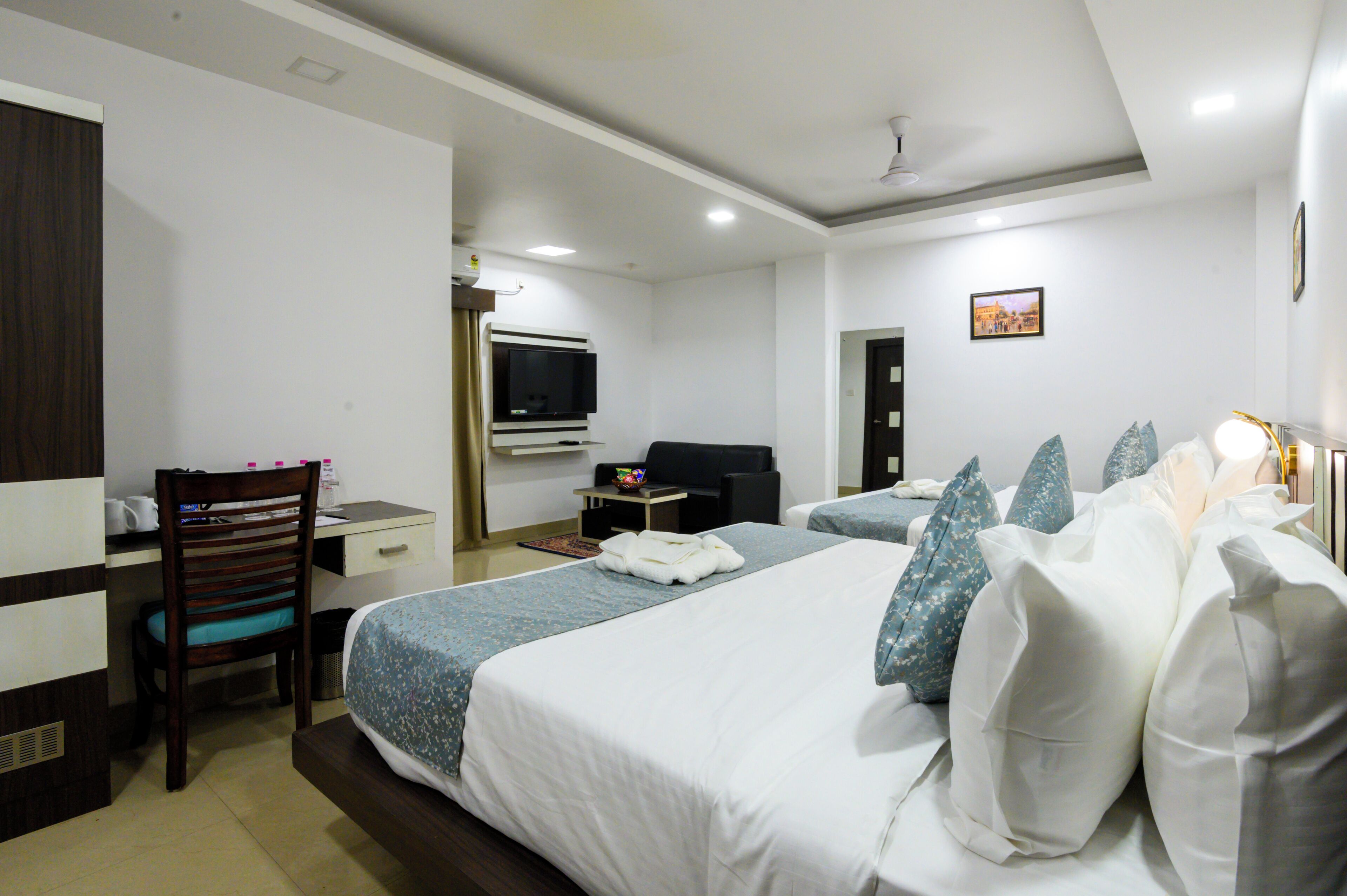 A hotel room with two beds, a desk, a chair, a television, and a small table.