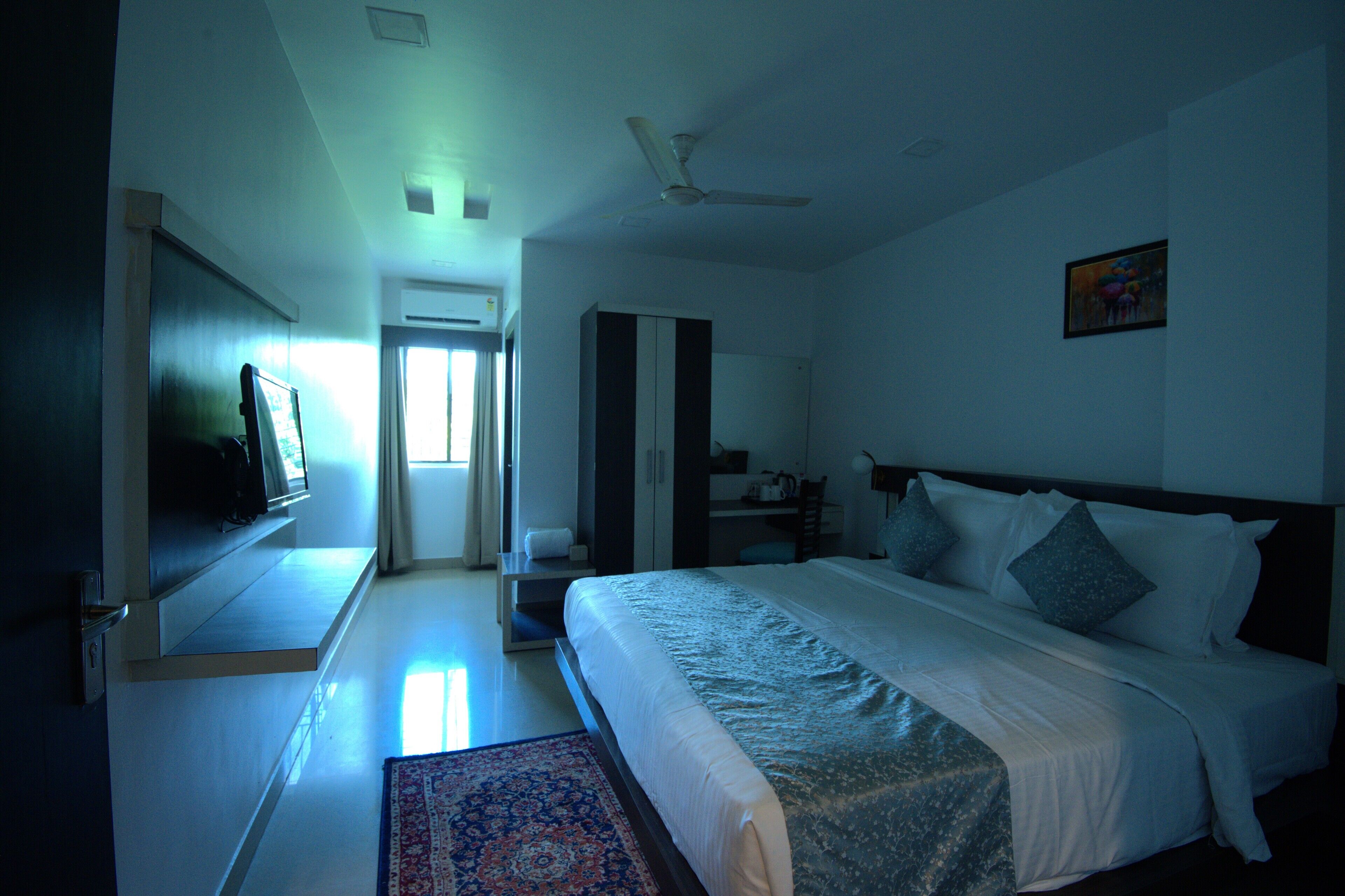 A hotel room with a bed, a television, a ceiling fan, and a window.