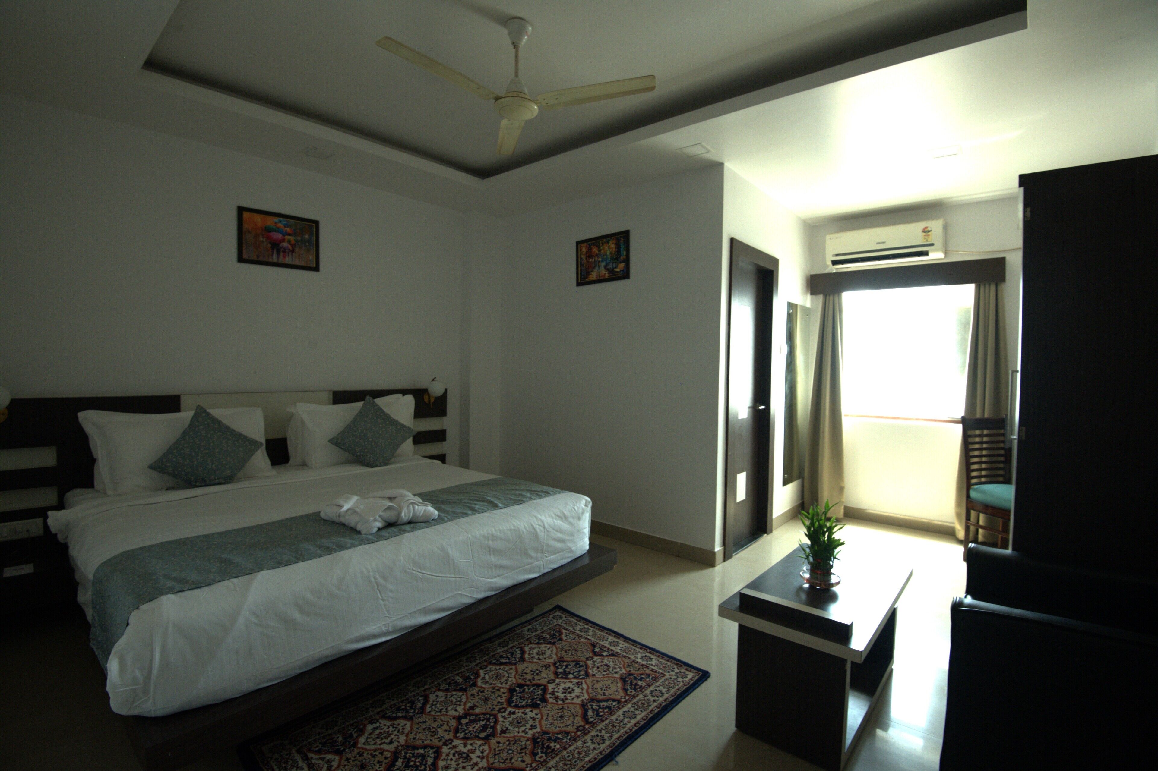 Habitación de hotel con una cama grande, ventilador de techo, aire acondicionado y vistas al balcón exterior.