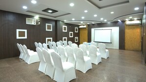 Un salón de conferencias con filas de sillas blancas, una pantalla de proyector y luces en el techo.