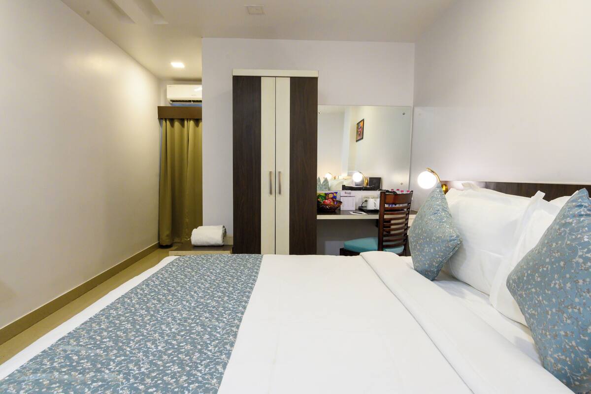 A hotel room with a bed, a wardrobe, a desk with a mirror, and a bathroom.