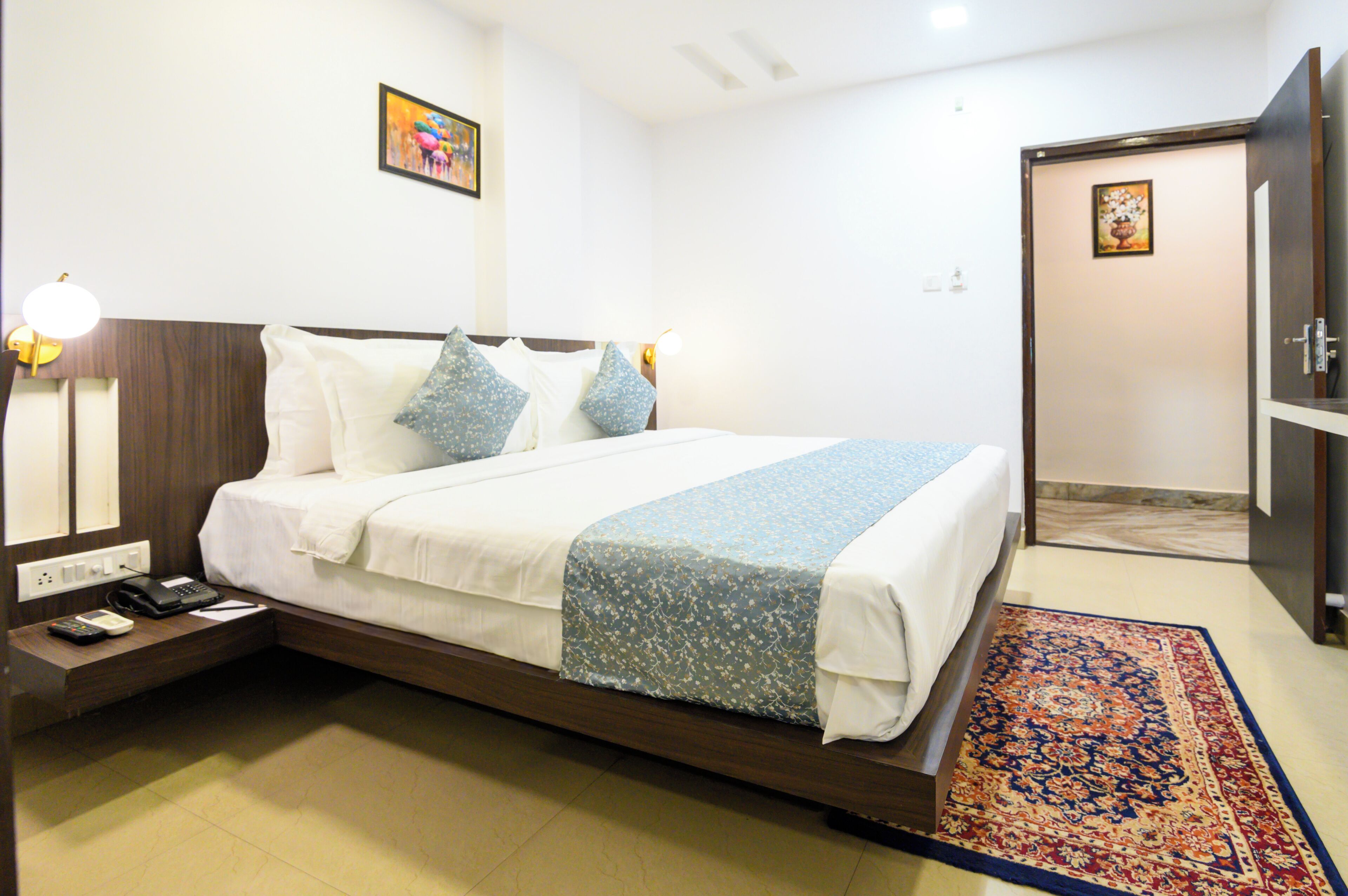 A hotel room with a bed, bedside tables, a nightstand, a rug, and a door.