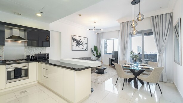 Een moderne keuken met een centraal eiland, een eethoek met een glazen tafel, en een zithoek met een bank en televisie.