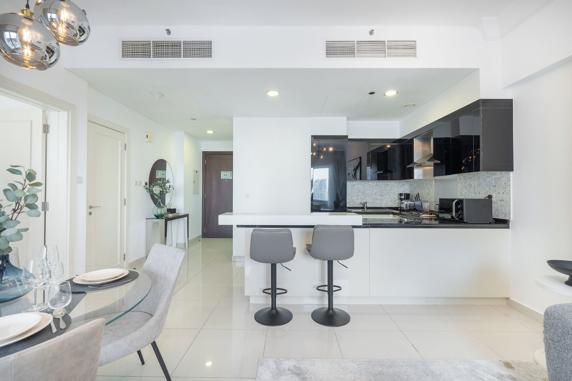 A modern kitchen with a central island, two bar stools, and a dining area with a glass table and chairs.