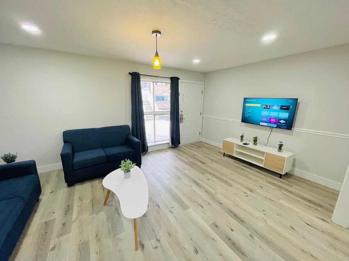 Uma sala de estar moderna com um sofá azul escuro, uma mesa de centro branca e uma TV fixada na parede.