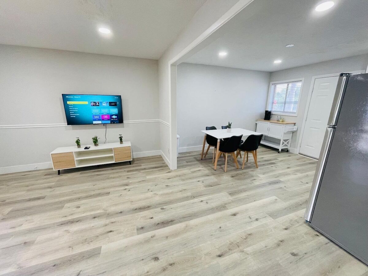 A modern kitchen with a built-in refrigerator, a dining area with a table and chairs, and a flat-screen TV mounted on the wall.