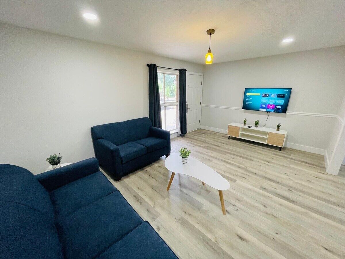 A modern living room with a blue sofa, a white coffee table, and a TV on the wall.