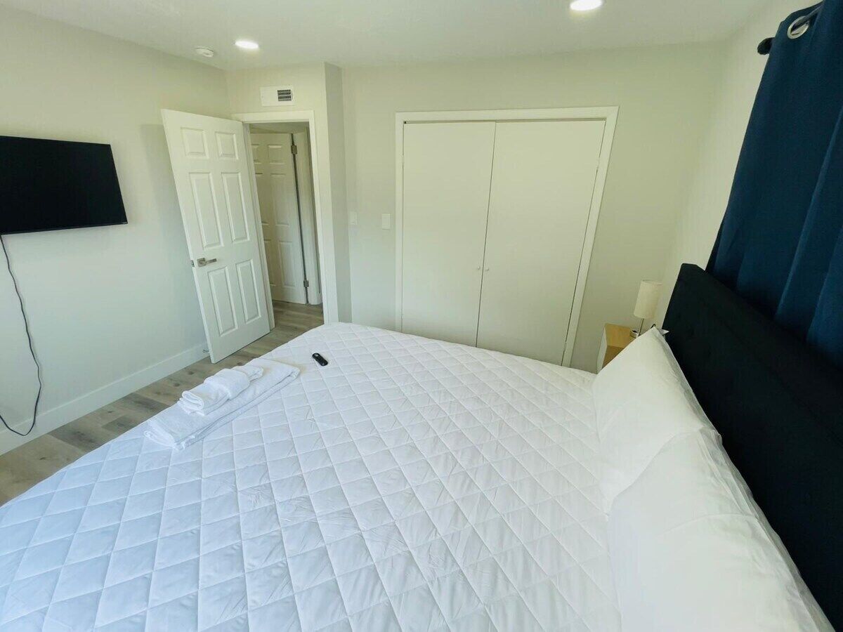 A hotel room with a large bed, a flat-screen TV mounted on the wall, a wardrobe, and a door leading to another room.