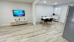 Une cuisine moderne dotée d’un réfrigérateur encastré, d’un coin repas avec une table et des chaises, et d’un téléviseur à écran plat fixé au mur.