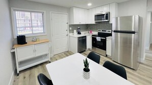 Une cuisine moderne avec des meubles blancs, des appareils en acier inoxydable et un coin repas comprenant une table et des chaises blanches.