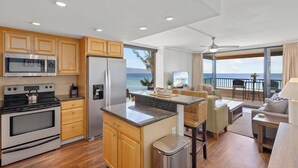 A modern kitchen with wooden cabinets, stainless steel appliances, and a view of the ocean.